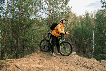 A male cyclist stands on a mountain in autumn with a mountain bike and enjoys the landscape