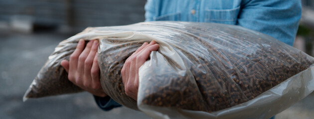 Man holding bag with wood pellets, pellet fuels manufactured in wood pellet line. Reusing wooden industrial waste. - obrazy, fototapety, plakaty