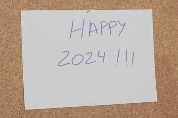 Message written with a pen on a white paper attached to a cork board with the message happy 2024