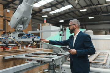 Male engineer in modern industrial factory, checking robotic arm, controling process and...