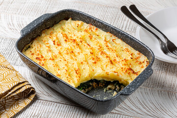 Creamy baked mashed potatoes with spinach, chicken meat and cheese in a casserole. White wooden table.