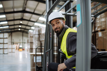 Portrait of warehouse worker driving forklift. Warehouse worker preparing products for shipmennt,...