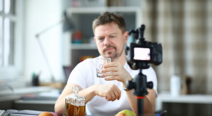 Exhausted man with black eye drinks alcohol in front of camera. Loneliness and alcoholism blogger...
