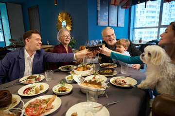 Cheerful women men little boy celebrating New Year with wine in restaurant