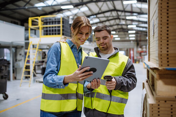 Young man with Down syndrome working in warehouse, female colleague teaching him scan products with...