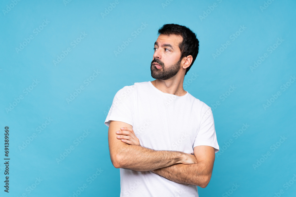 Wall mural Young man with beard  over isolated blue background with confuse face expression