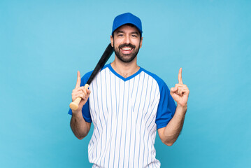 Young man playing baseball over isolated blue background pointing up a great idea