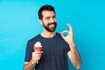 Young man with a cornet ice cream over isolated blue background showing ok sign with fingers