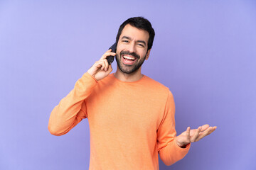 Caucasian handsome man over isolated purple background keeping a conversation with the mobile phone with someone