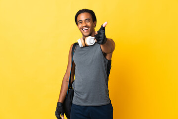 Young sport African American man with braids with bag isolated on yellow background with thumbs up because something good has happened