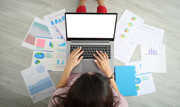 Freelancer using laptop next to papers with charts sitting on floor top view. Remote work telework and preparation of report analytics