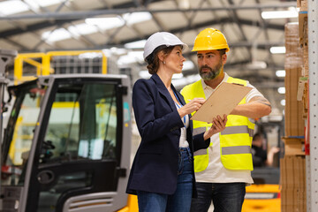 Forklift driver talking with manager in modern industrial factory. Warehouseman reading order, order picking. Warehouse worker preparing products for shipmennt, delivery, checking stock in warehouse. - obrazy, fototapety, plakaty