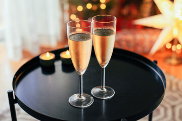Two glasses of white sparkling wine on a black table. Cosy Christmas atmosphere with lights, tree,...