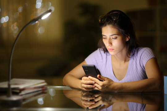 Woman checking cell phone on a desk in the night at home