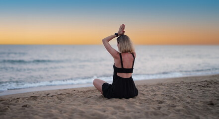 Fototapeta na wymiar Woman doing yoga on seashore at sunset back view. Calmness and relax concept