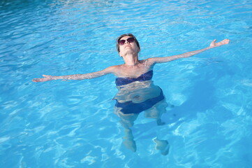 Young woman in sunglasses swimming and relaxing in pool top view. Vacation at resort concept