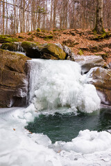frozen cascade of a forest water stream among boulders. frosty but winter scenery of carpathian...
