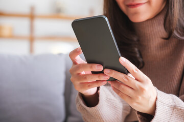 Closeup image of a young woman holding and using smart phone at home