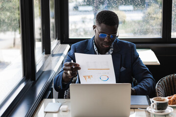 Black businessman sitting in a coffee shop, working with his laptop