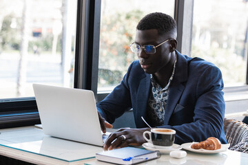 Portrait of black man working on laptop computer in busy cafe
