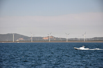 船から見た風力発電の塔と、その前を通り過ぎるボート