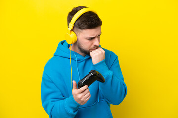 Young caucasian man playing with a video game controller isolated on yellow background having doubts