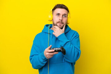 Young caucasian man playing with a video game controller isolated on yellow background having...
