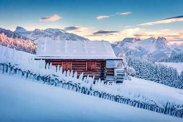 Wooden chalet on the hill of Alpe di Siusi village. Snowy winter sunrise on Dolomite Alps....