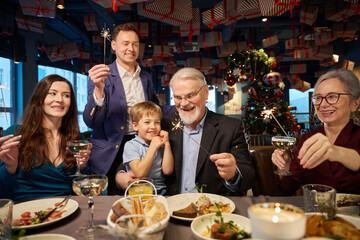 Family hold Bengal lights and glasses with champagne during New Year celebration