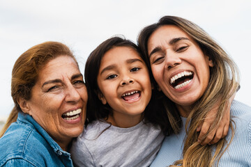 Happy Hispanic multigenerational family smiling into the camera - Child having fun with her mother and grandmother outdoor - obrazy, fototapety, plakaty