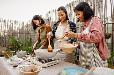 Southeast asian mother with her daughters having fun preparing Thai food recipe together at house...