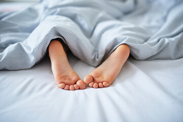 Little child's feet in bed covered with blanket - obrazy, fototapety, plakaty