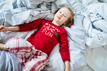 Happy preschooler girl wearing Christmas pajamas, playing on bed