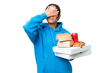 Young Uruguayan woman holding pizzas and burgers over isolated chroma key background covering eyes...