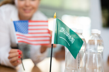 Little flag of Saudi Arabia on table with bottles of water and flag of the USA put next to it by...