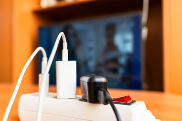 Electricity price concept.Electric power plugs in foreground at home,blurred TV.Concept of expensive electricity costs and rise in energy bill prices.