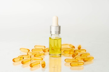 Oil capsules and serum bottle with dropper on white background. Nutritional supplement contains...
