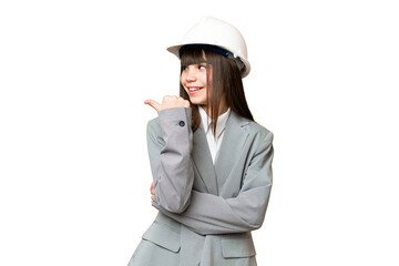 Little girl playing as a architect with helmet and holding blueprints over isolated background pointing to the side to present a product