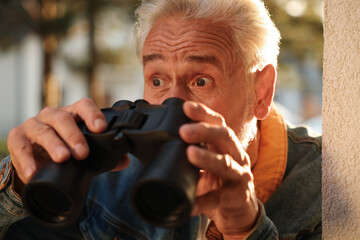 Concept of private life. Curious senior man with binoculars spying on neighbours outdoors, closeup