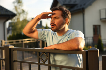 Concept of private life. Curious man spying on neighbours over fence outdoors