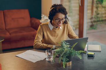 Smiling female business analyst working remotely on laptop from home while sitting at living room