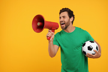 Emotional sports fan with soccer ball and megaphone on orange background
