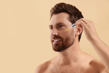Obraz premium Smiling man applying cosmetic serum onto his face on beige background, closeup. Space for text