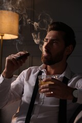 Handsome man with glass of whiskey smoking cigar at home