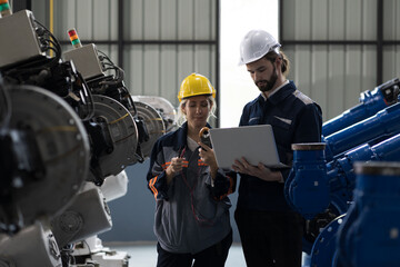 Male and female engineer working in autonomous robotics warehouse storage, using laptop computer and inspecting quality of robot parts. Industrial manufacturing by robotic arms concept