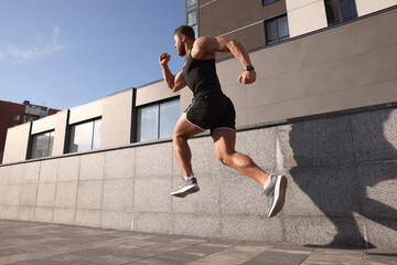 Young man running near building outdoors, low angle view. Space for text