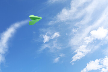 Green paper plane flying in blue sky with clouds
