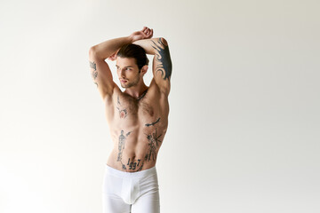 sexy alluring man with ponytail and cool tattoos in comfy underwear posing on ecru background