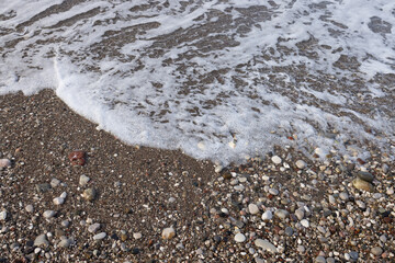 Lace foam of the sea wave on a pebble beach