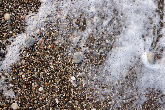 Small colorful pebbles on the beach, covered with foam. View from above © Anna